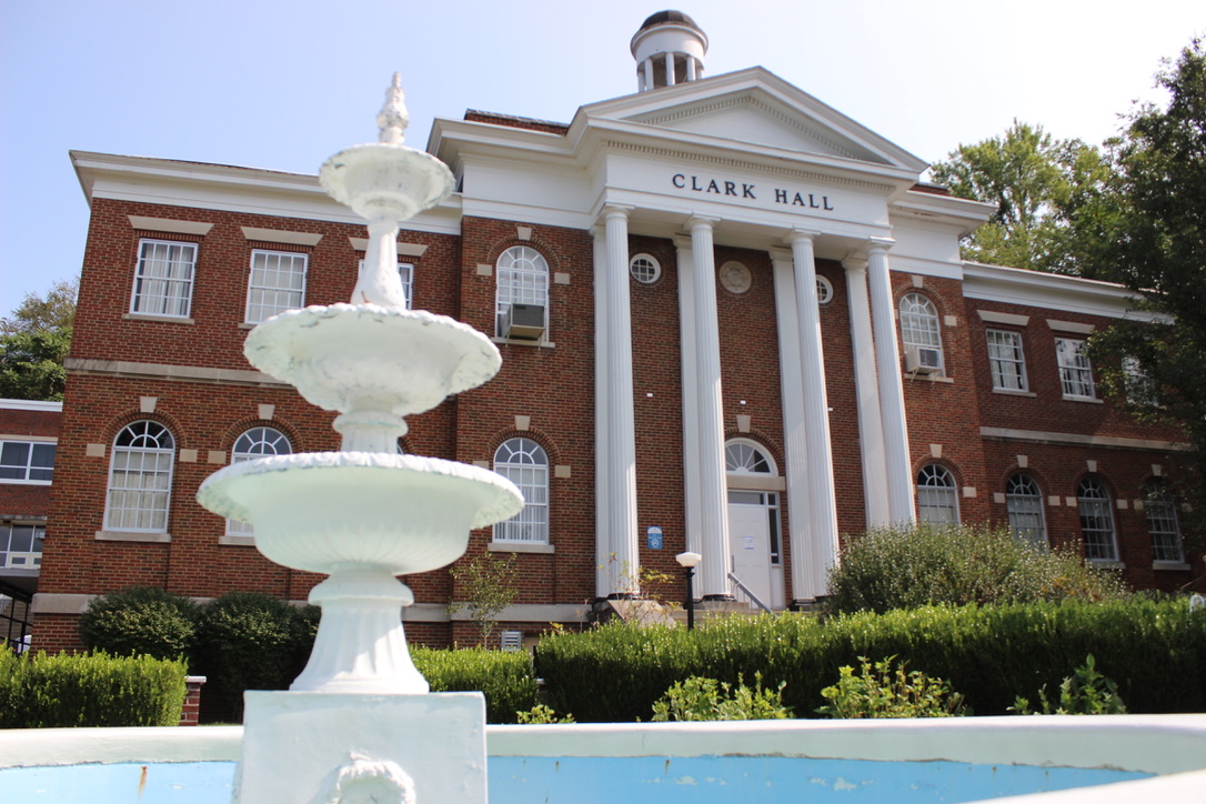 Image: A front view of Clark Hall, a large brick building with tall white pillars and arched windows. In front of the building stands a three-tiered fountain.