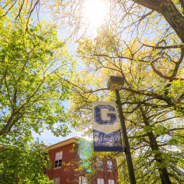 Bright green tree leaves frame a brilliant blue Glenville State College banner