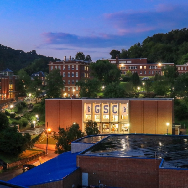 A wide shot of campus at night, with glowing lights emanating from the windows of buildings across campus. In the center of the picture, three large banners, imprinted with "G", "S", and "C" hang illuminated.