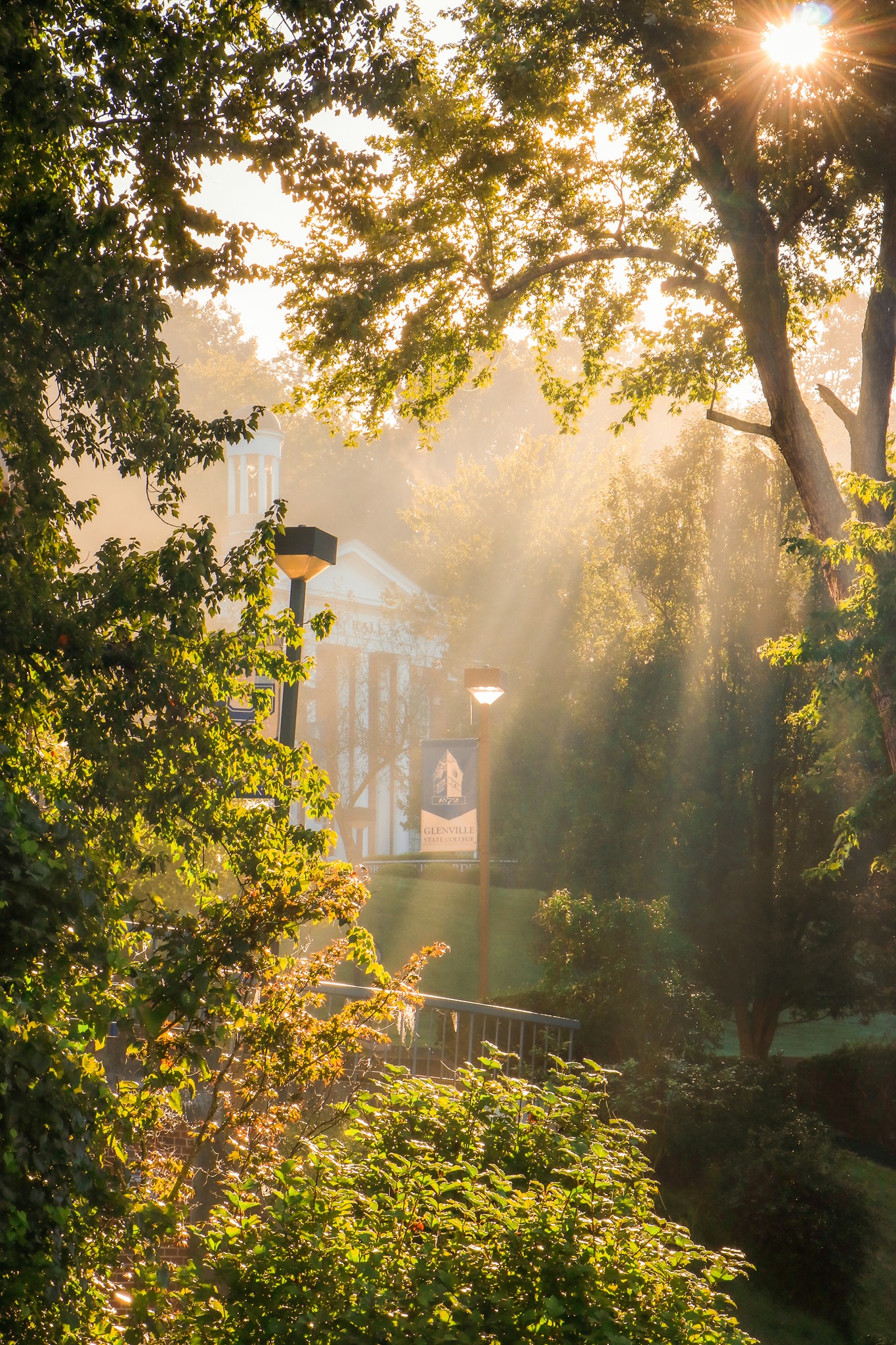 Clark Hall stands in the distance, bathed in soft early morning sunlight. Lush green and golden trees frame the shot.