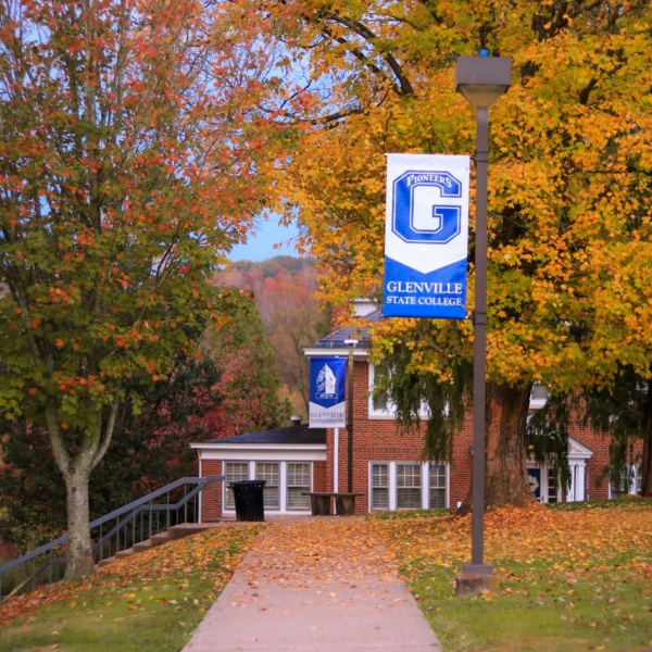 Brilliant yellow, orange, and red trees line a campus walkway which features lamp posts hung with bright blue GSC banners.