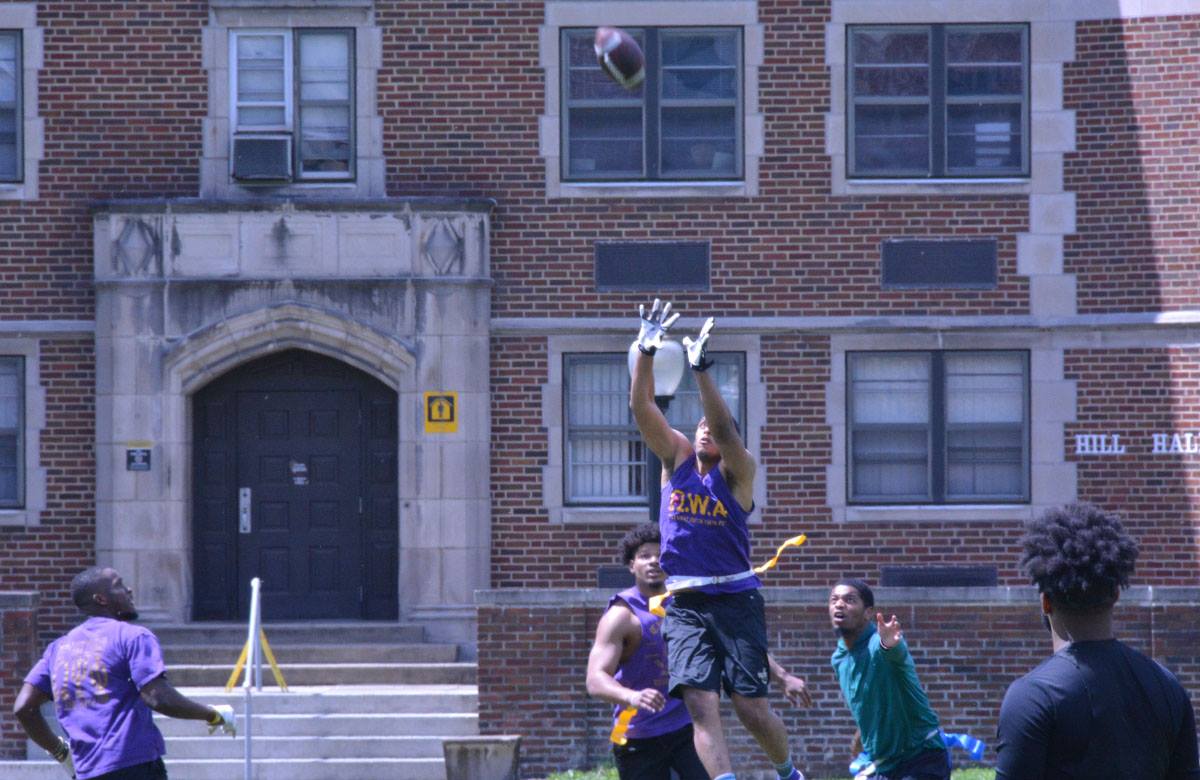 A group of students play football on the quad. One student leaps in the air to catch the ball.