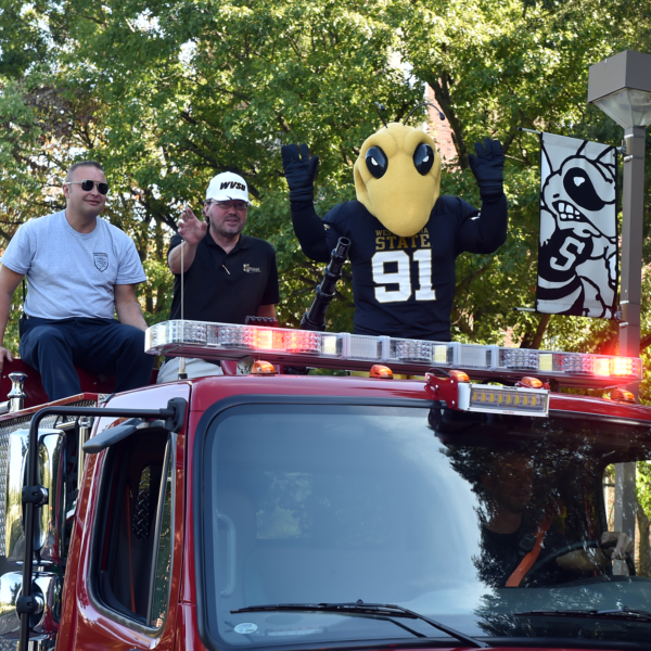 WVSU Mascot rides with two men on a firetruck.