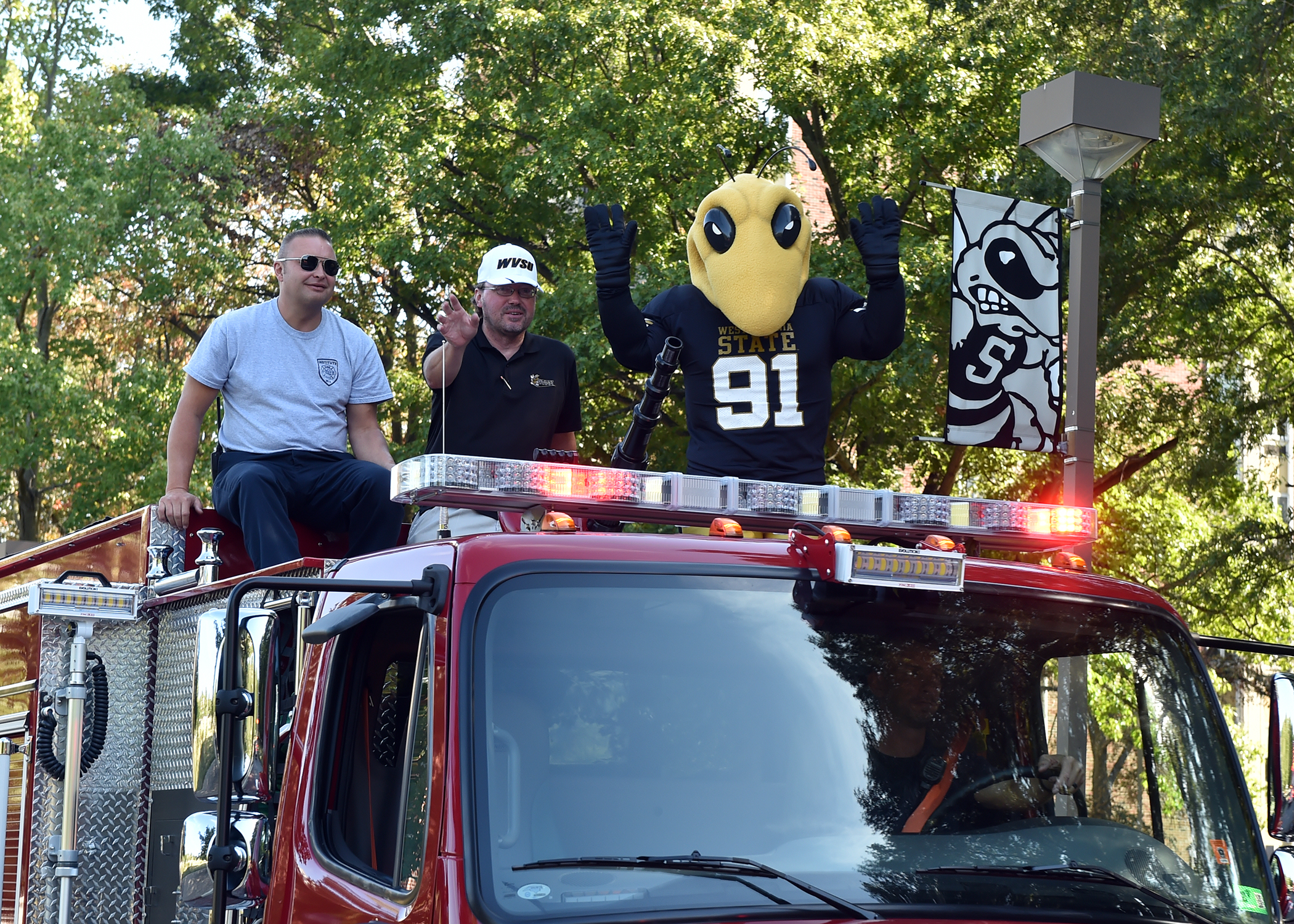 WVSU Mascot rides with two men on a firetruck.