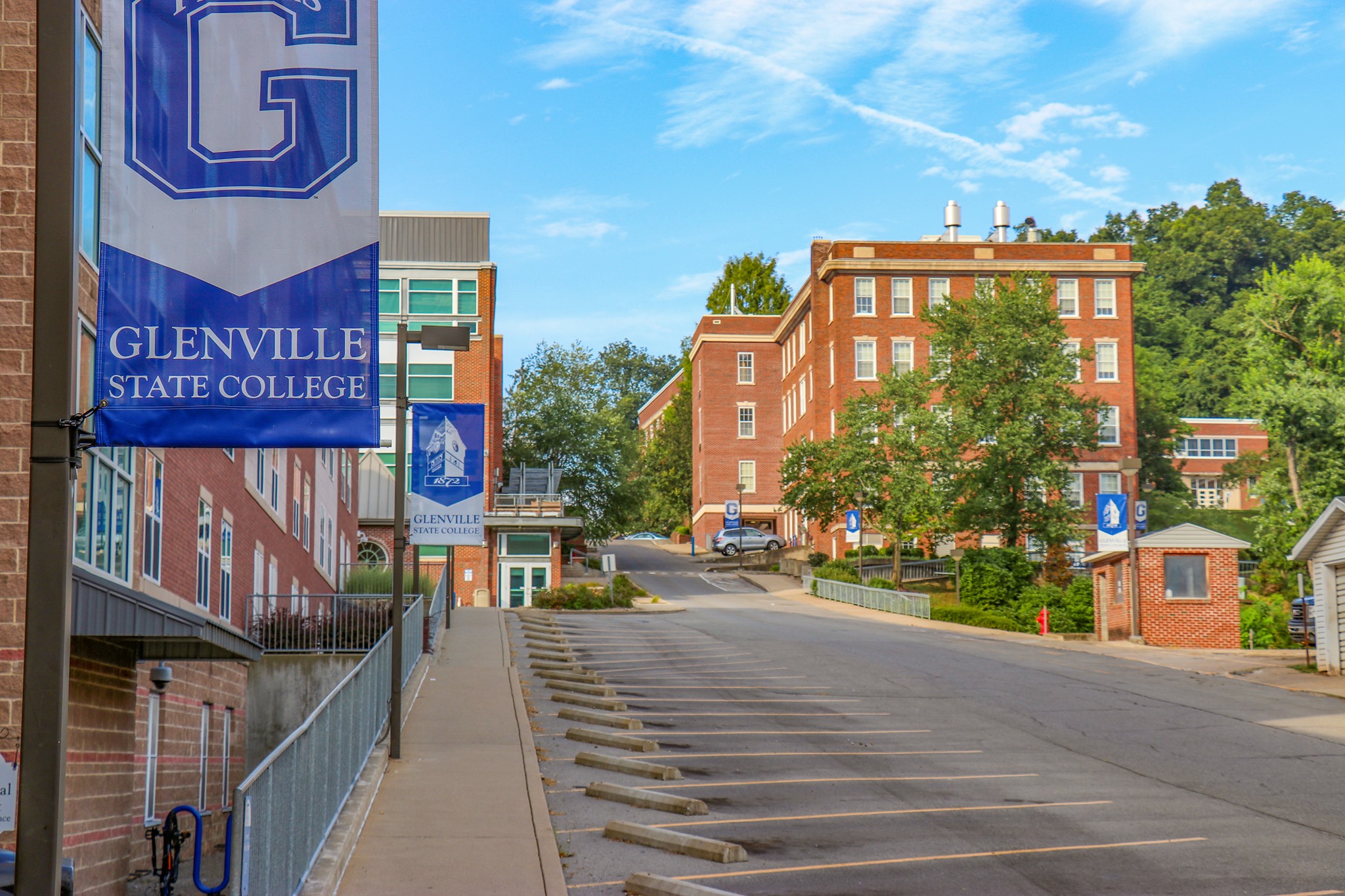 A view of campus from just outside of Goodwin Hall. The shot shows the main street, lined with bright blue GSC banners. It's a bright summer day.