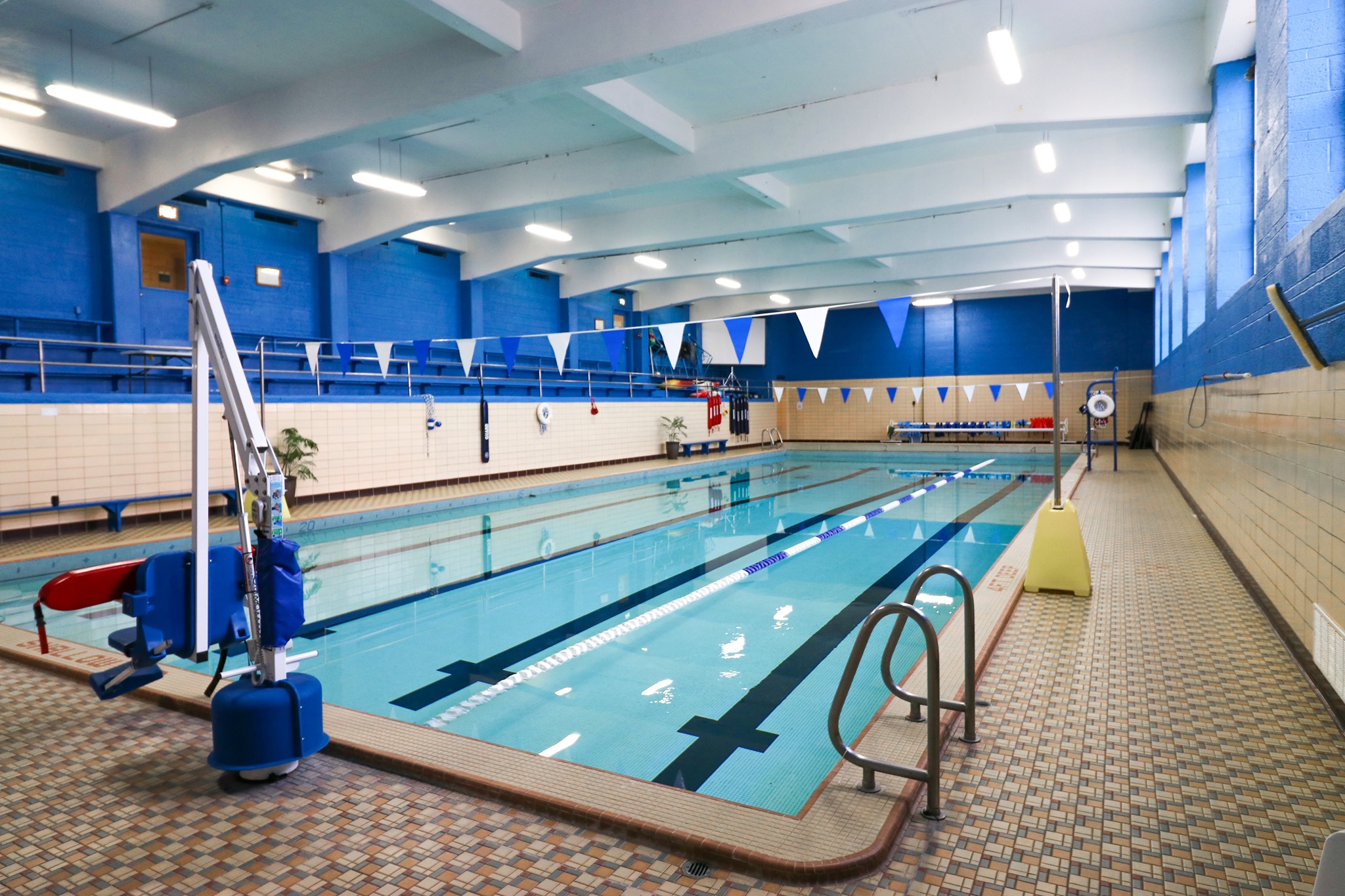 An indoor swimming pool divided into swim lanes with blue and white flags hanging above the pool.