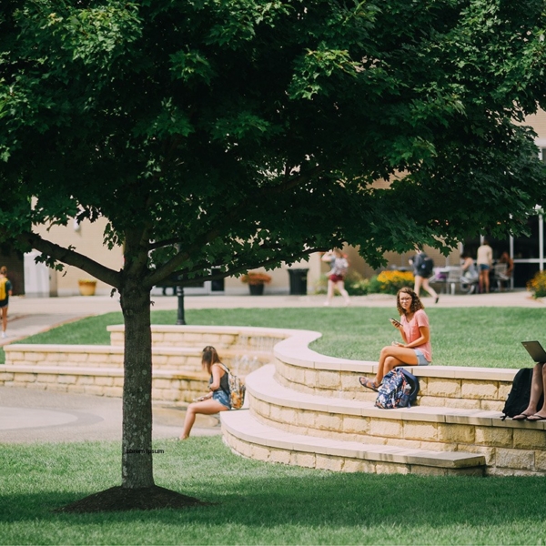 A group of students sit on amphitheater-style benches surrounding a modern-looking water fountain.