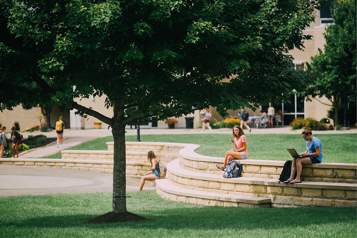 A group of students sit on amphitheater-style benches surrounding a modern-looking water fountain.