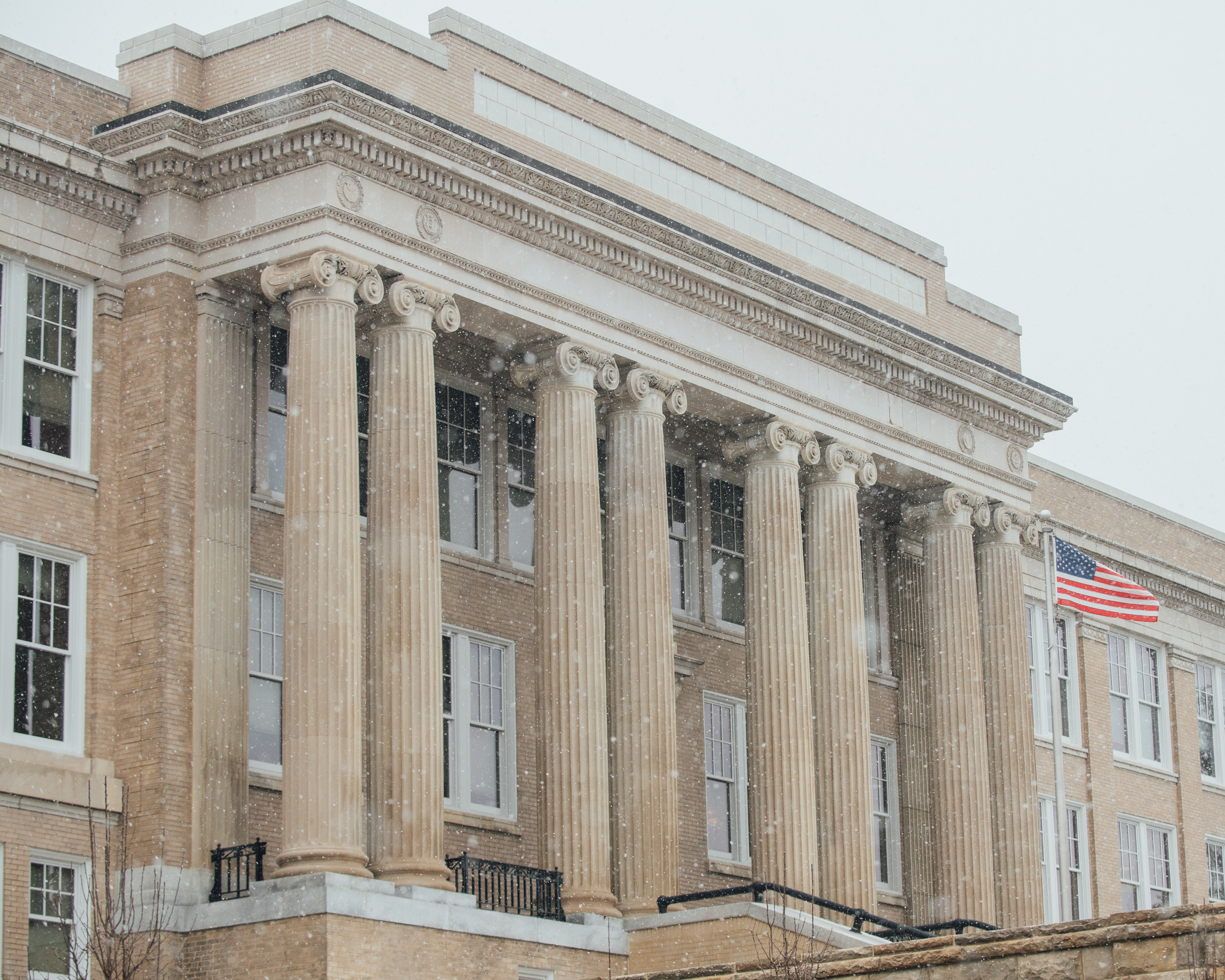Soft snowflakes fly in front of a classical-looking building with huge stone columns
