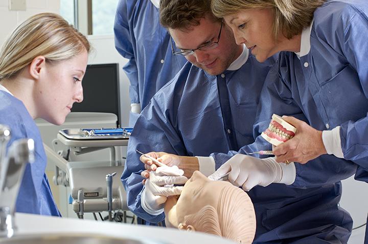 Three dental hygiene students work with an instructor and practice teeth cleaning techniques mannequin.