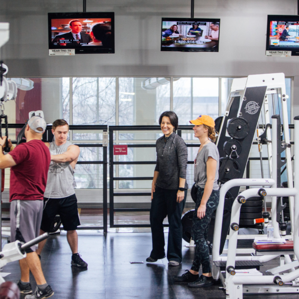 Students use a variety of weight training equipment in a modern-looking indoor gym.