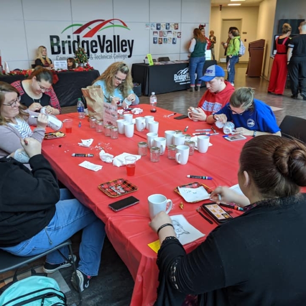 Students gather around tables in the Building 2000 lobby to decorate mugs with holiday designs.