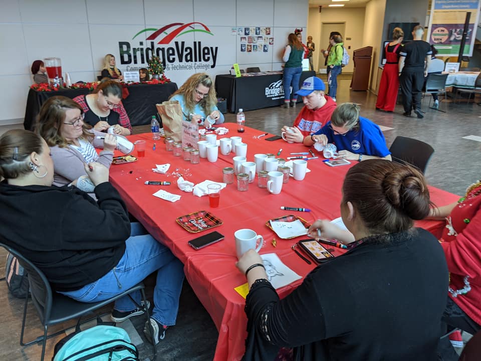 Students gather around tables in the Building 2000 lobby to decorate mugs with holiday designs.