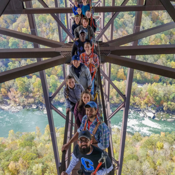 Image: Smiling Glenville State College students pose for a photo on the New River Gorge Bridge Catwalk, a walkway running beneath the bridge. Far below, you can see the New River.