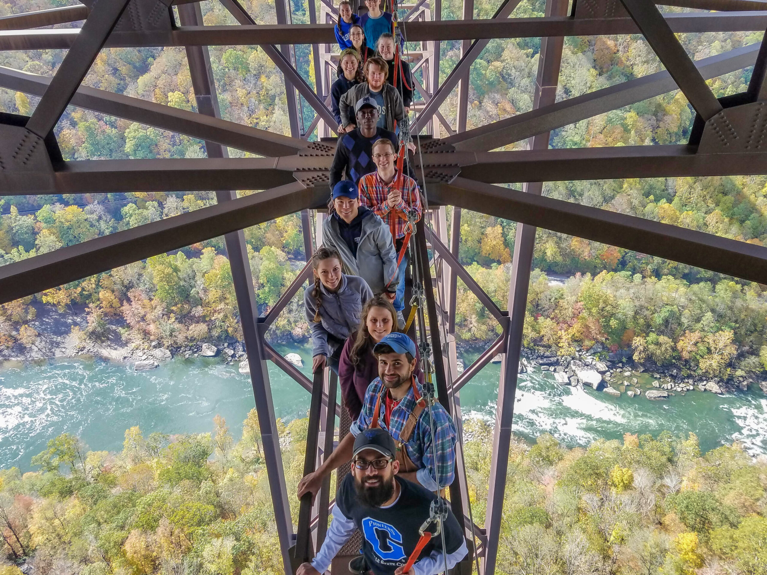 Image: Smiling Glenville State College students pose for a photo on the New River Gorge Bridge Catwalk, a walkway running beneath the bridge. Far below, you can see the New River.