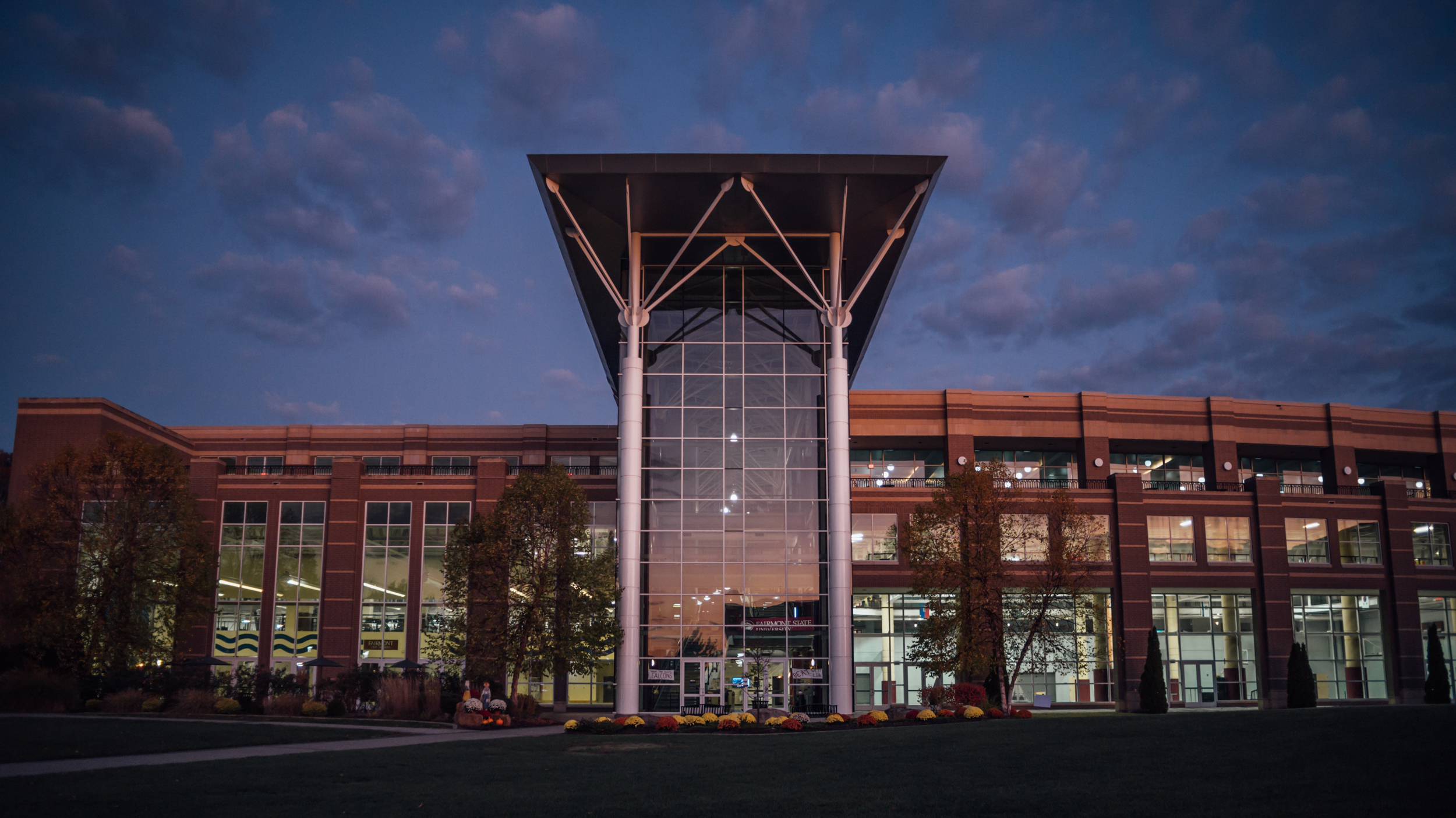 A front view of the Falcon Center, a huge structure with floor to ceiling glass. Here, the building is pictured at night with soft lights glowing inside and reflecting in the windows.