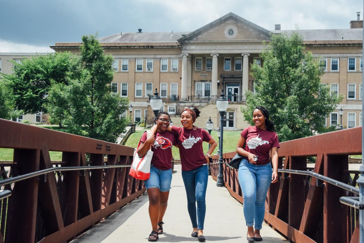 Three female students smile as they walk across the bridge in front of Morrow Hall