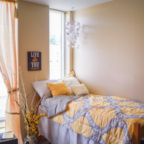 An airy bedroom featuring a twin bed, a chair, flowers, and floral curtains